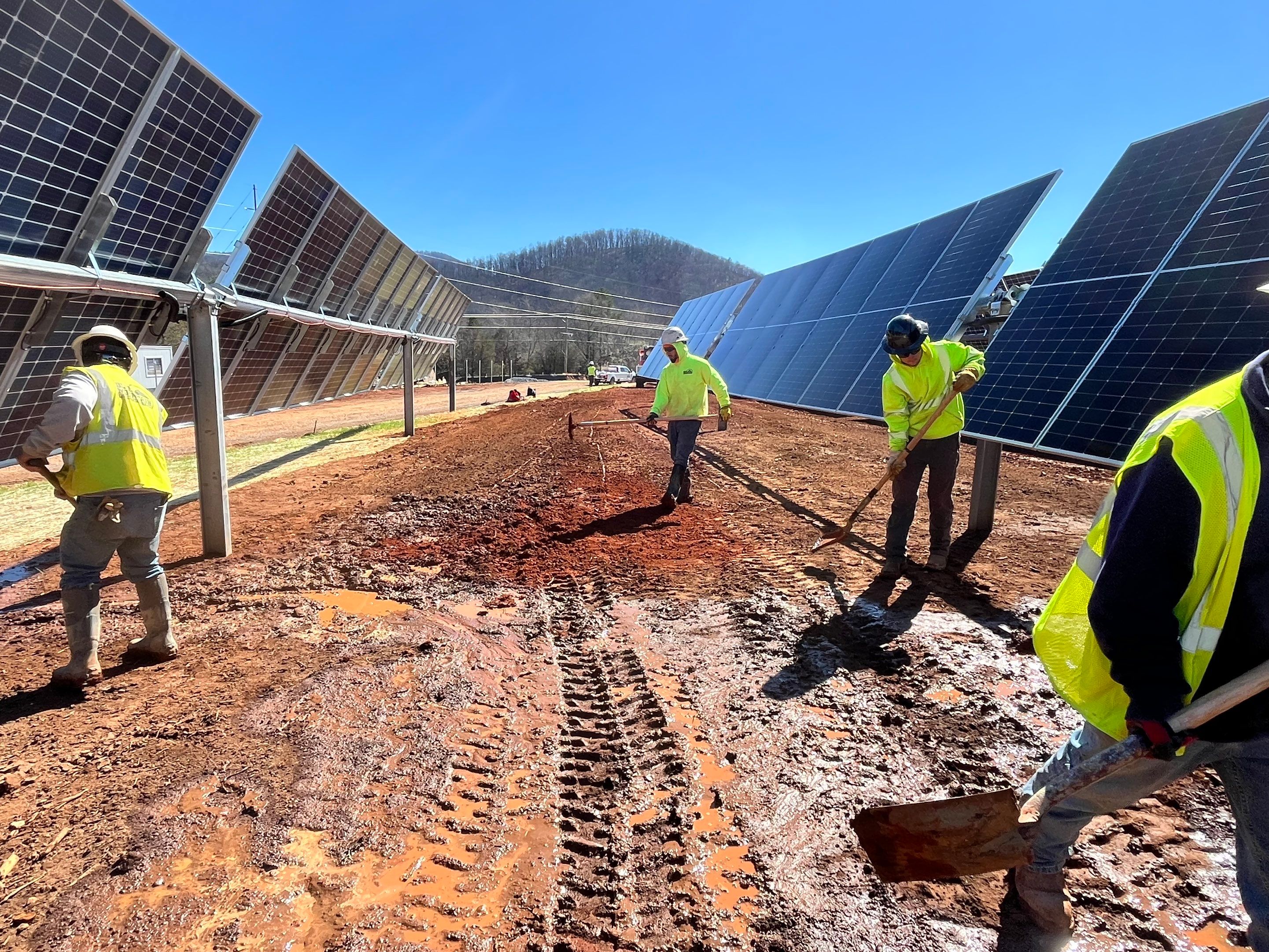 Crew members working between solar panel rows on a muddy site